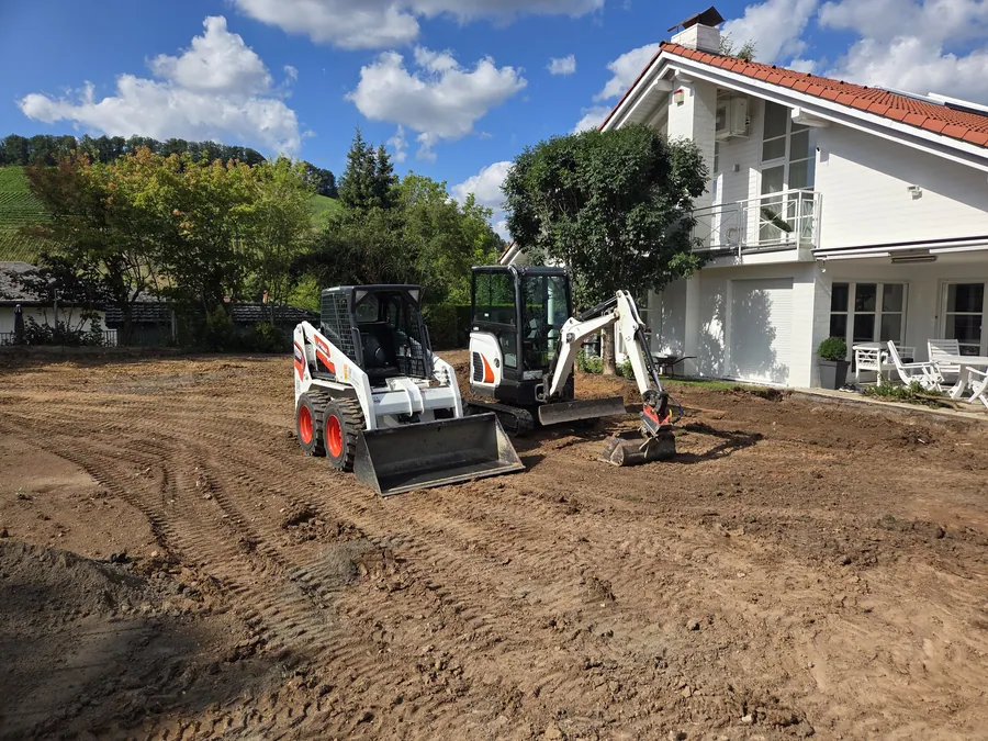 Minibagger hebt eine Betonplatte am Hauseingang an einem Anschlagmittel